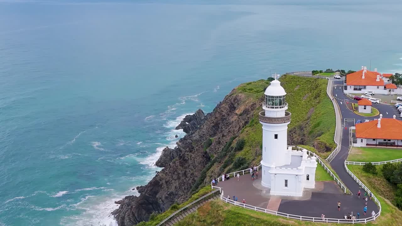 Aerial view of a lighthouse perched on green cliffs with ocean waves below.