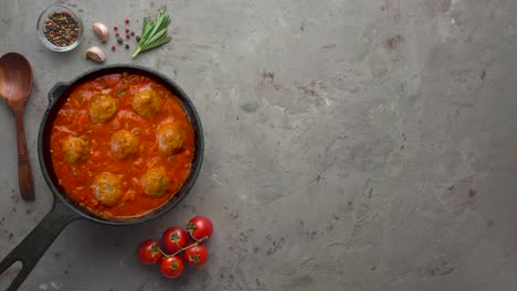 cooking meatballs with tomato sauce in black pan. flat lay, top view with copy space