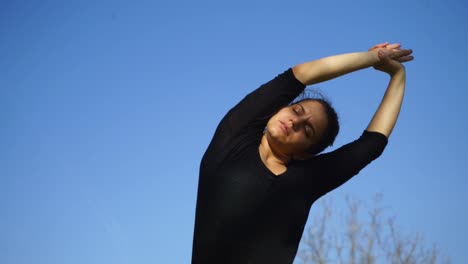 sportive young woman with closed eyes stretching against blue sky