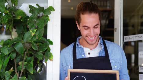 Portrait-of-smiling-waiter-showing-chalkboard-with-open-sign