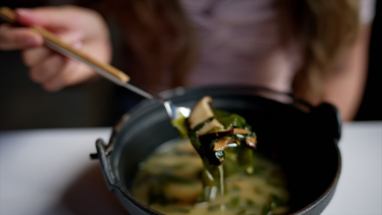 Woman eating japanese seaweed miso soup with tofu cheese, slow motion stir