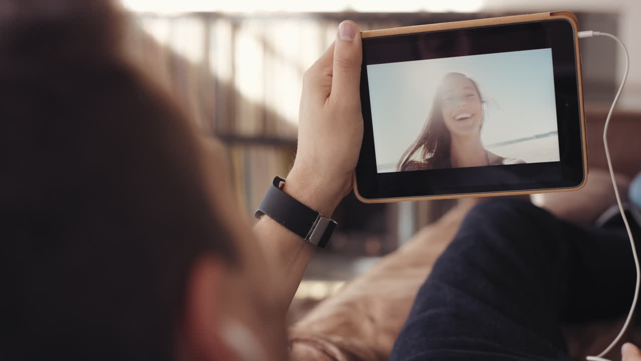 un tipo genial hablando con su novia en una aplicación de video de internet usando un sofá de tableta digital en casa.