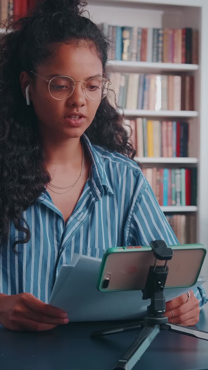 Young woman online educator records video lesson at home library using tablet