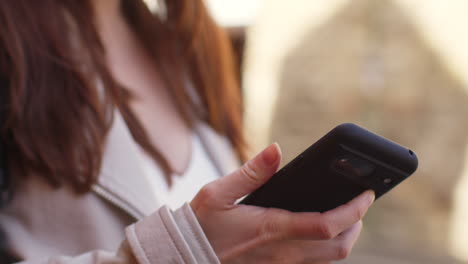 Close-Up-Shot-Of-Woman-Outdoors-On-City-Street-Holding-Mobile-Phone-Looking-At-Messages-Social-Media-Or-News