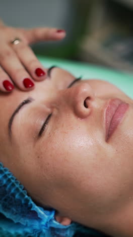 bare hands of cosmetologist cover woman's face with transparent gel. beauty and skincare concept. salon procedures. close up. vertical video