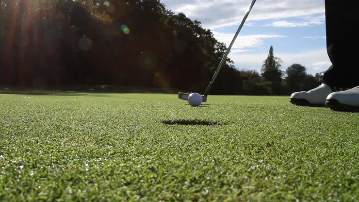 Ripresa statica a livello del suolo di un golfista che imbuca, imbucando verso la telecamera con bagliore dell'obiettivo