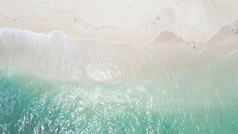 top down aerial view of crystal clear sea water and white sand beach