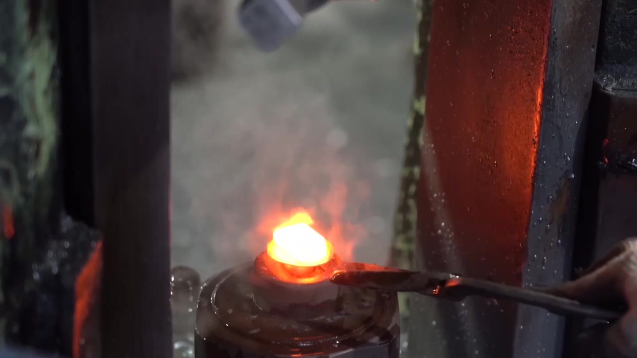 Hammer press striking a glowing orange steel blank inside a forging die