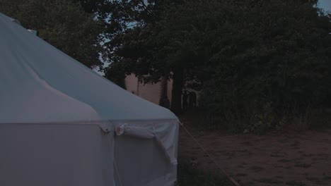 white tent set-up at foreground of a manor home with kids playing through dusk. - static shot