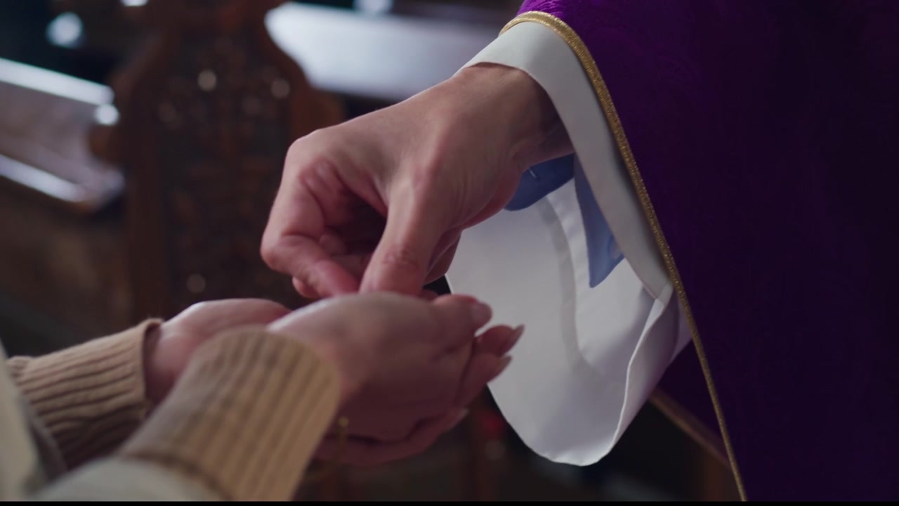Sacerdote che pone l'ostia nel palmo della mano della donna che riceve la comunione e lei che prende l'eucaristia.