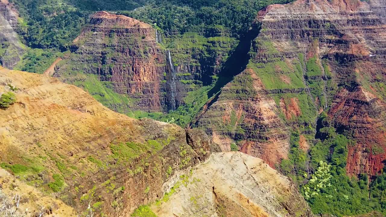 hd hawaii kauai tiro amplio estático en cámara lenta del cañón de waimea con una cascada en la distancia y un helicóptero entrando en el cuadro volando a la derecha pasando por la cascada