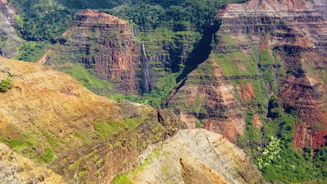 HD-Hawaii-Kauai-slow-motion-static-wide-shot-of-Waimea-Canyon-with-a-waterfall-in-distance-and-a-helicopter-entering-frame-right-flying-past-waterfall