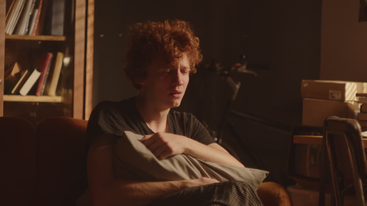 hombre estresado abrazando almohada y mordiendo su brazo mientras llora en casa