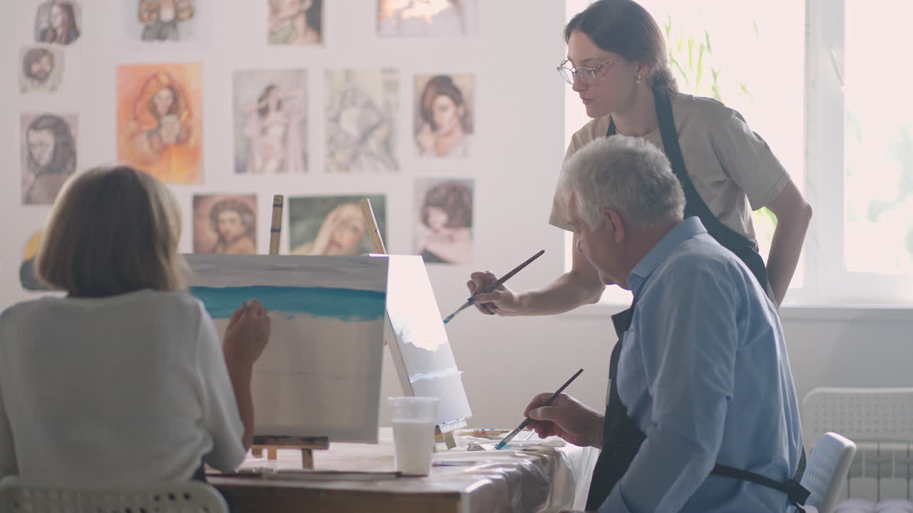 vista de ángulo alto de amigos mayores alegres pintando en lienzo. mujer mayor sonriendo mientras dibuja con el grupo. mayores asistiendo a clase de pintura juntos. hombres mayores divirtiéndose pintando en clase de arte