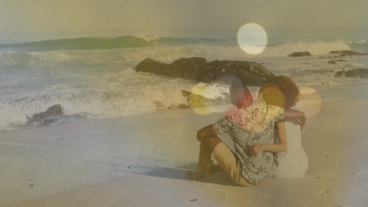 On sandy beach, couple watching colorful light animation with ocean waves nearby