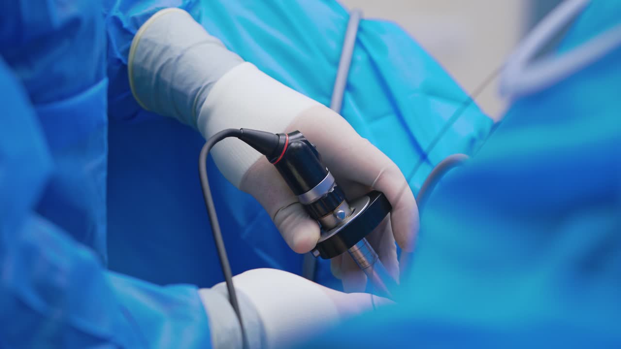 Innovative equipment during surgery. Doctor's hands in sterile gloves holding special instrument while perform an operation. Close-up. New technologies in medicine.