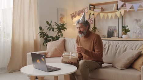 hombre celebrando un cumpleaños en línea usando sombreros de cumpleaños y abriendo un regalo