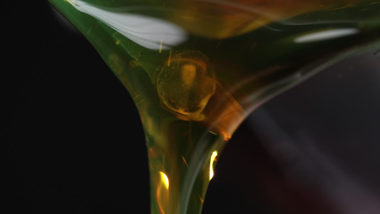 Pouring amber color motor oil from bottle on dark background