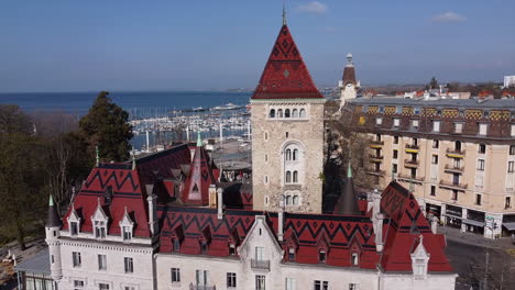 Slow-aerial-orbit-shot-of-a-large-hotel-built-on-the-site-of-an-old-medieval-castle-in-Lausanne,-Switzerland-on-a-sunny-day-with-Lake-Geneva-in-the-background