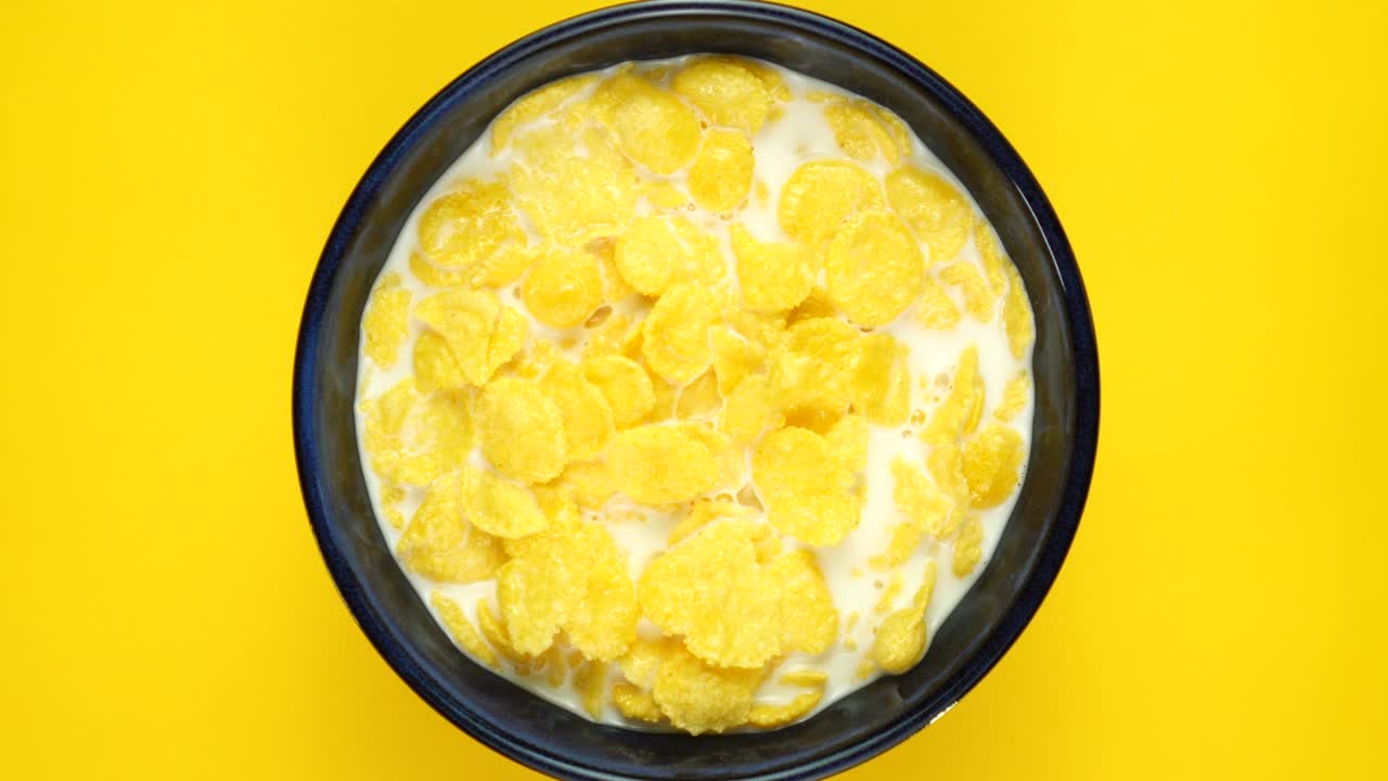 Goldene Cornflakes mit Milch rotieren auf gelbem Hintergrund. Draufsicht.