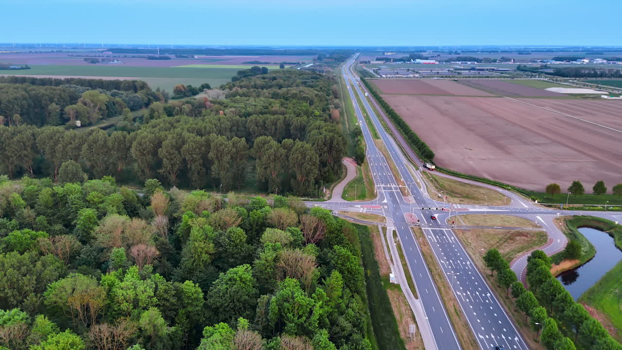 Modern highway along the agricultural field and deep wood. Drone flight over the countryside away from a big city.