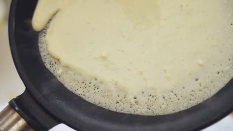 anonymous person putting the dough for a pancake in the pan