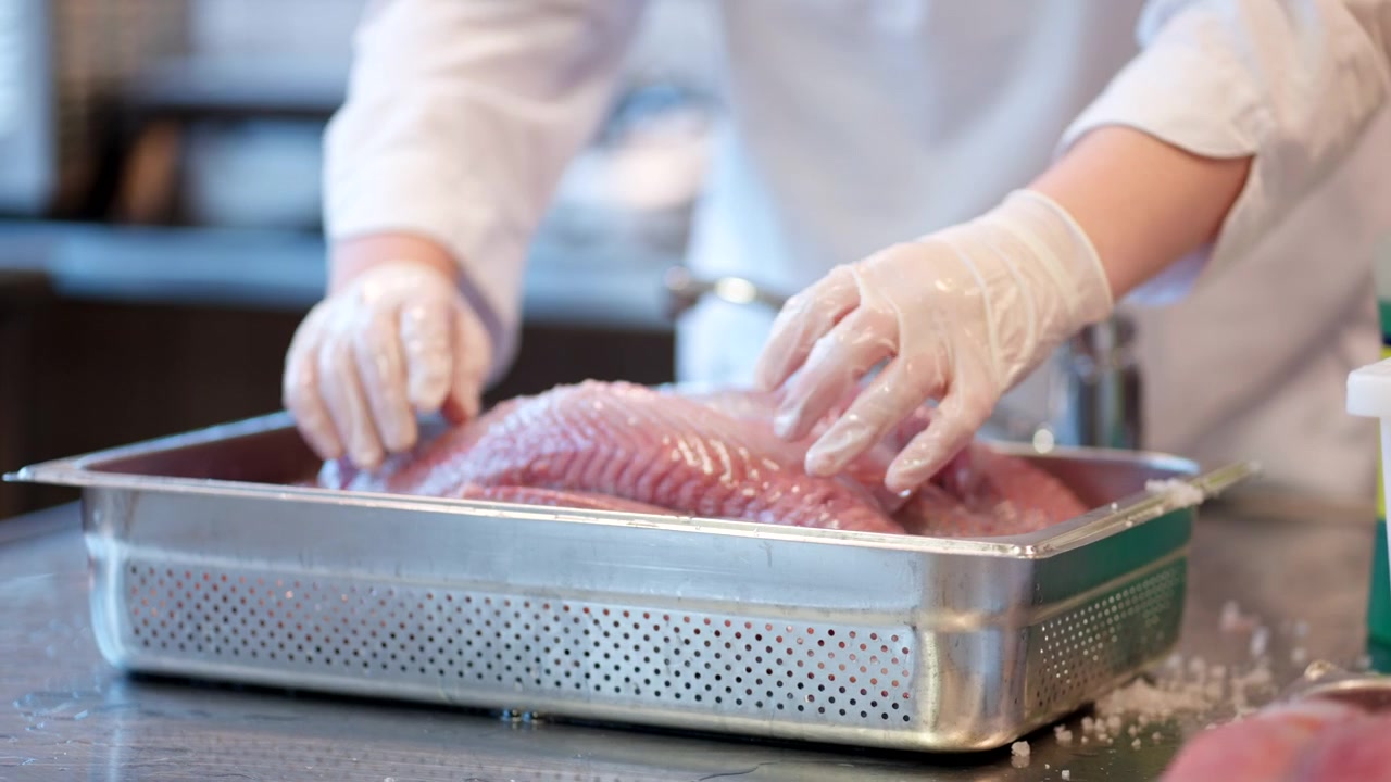 Washing salted herring under running water in a professional kitchen during seafood preparation, focus on container