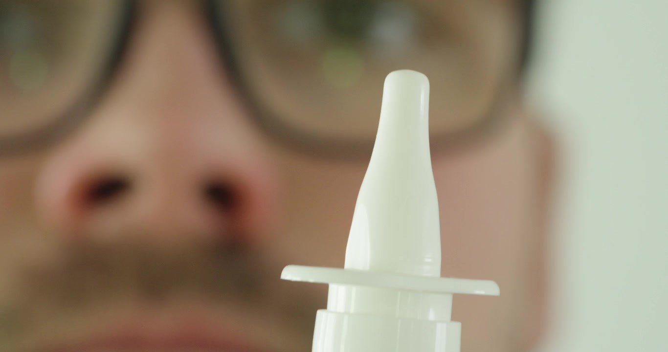 Vista macro estrema di un applicatore di spray nasale con un uomo e un naso sfocati sullo sfondo. Concetto di cura nasale, trattamento delle allergie, salute respiratoria, farmaci e assistenza sanitaria