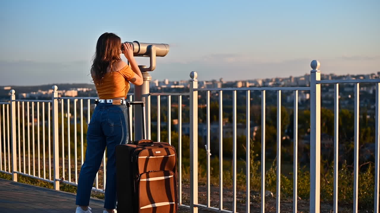 Young woman in protective medical mask looking into a tower viewer from the observation deck at the city at sunset. Corona Virus idea. Safe travel during the pandemic. Slow motion. Chisinau, Moldova
