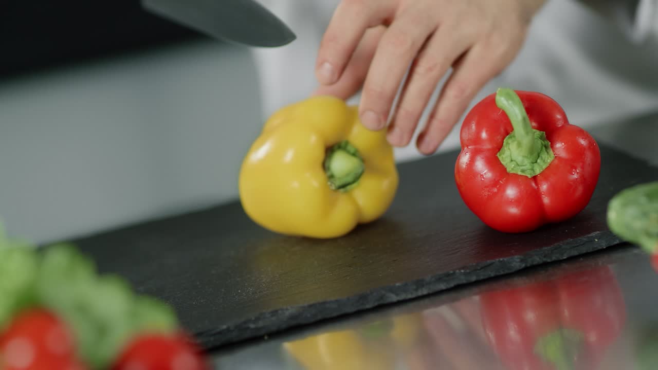 Šéfkuchař vaří jídlo v kuchyni restaurace. Detail rukou šéfkuchaře, které krájí žlutou papriku.