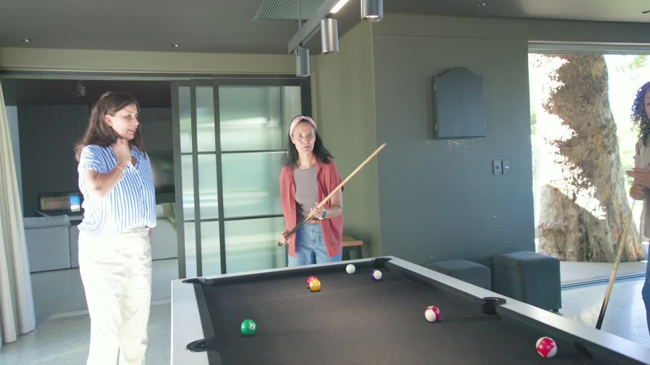 Female friends celebrating shot, regrouping, lining, shooting, watching balls at pool table playing