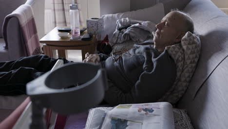 elderly man resting on couch with newspaper and crutches
