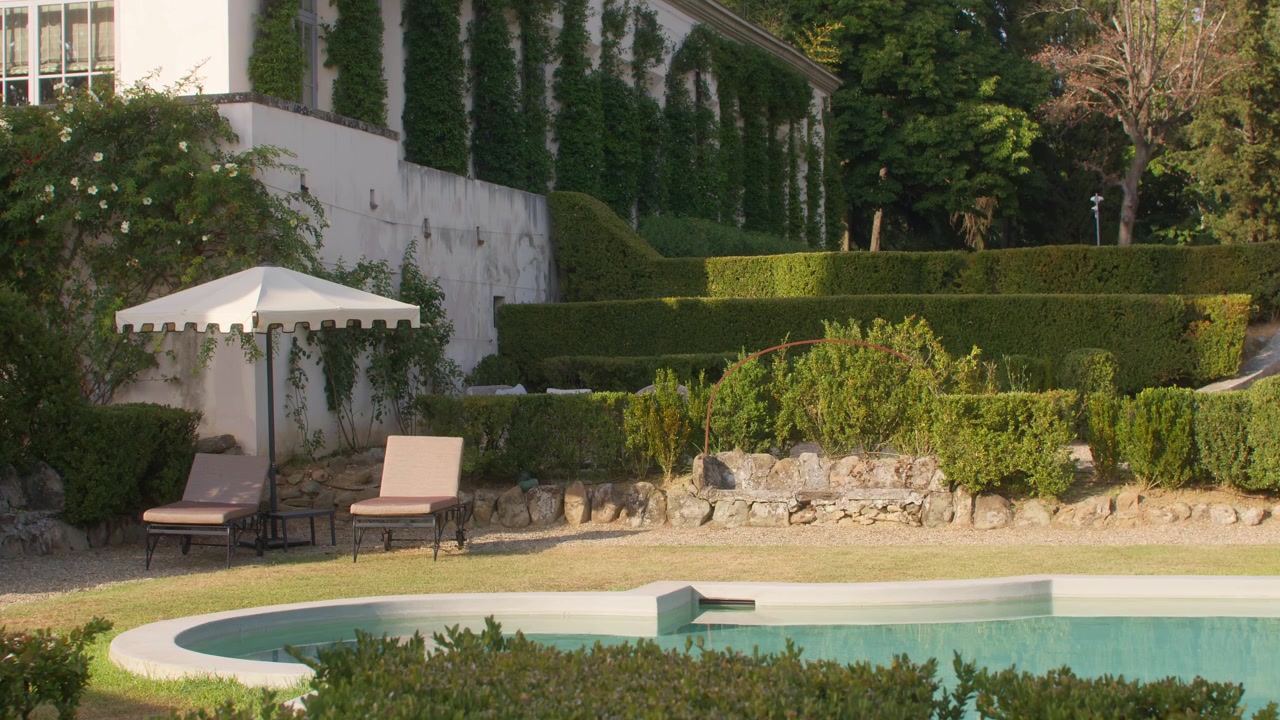 Elegante giardino di villa con siepi potate, piscina e lettini sotto il sole estivo