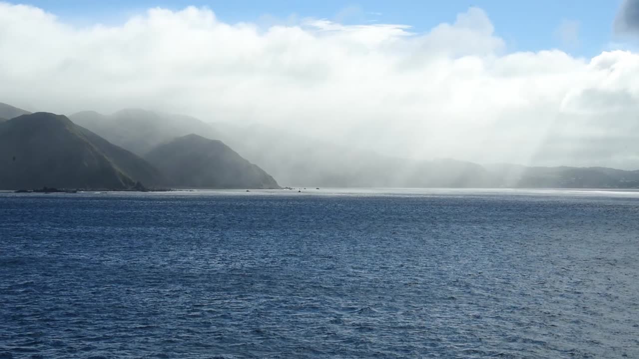 Dramatic clouds above the southern end of New Zealand North Island. Rain in the distance of the cliffs at the coast
