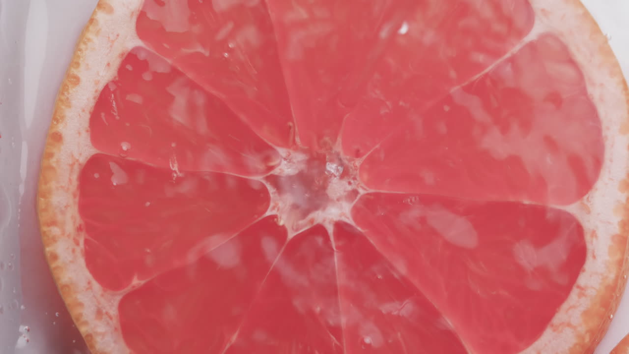 video de gotas de agua cayendo en una rebanada de pomelo rojo con espacio de copia en un fondo blanco