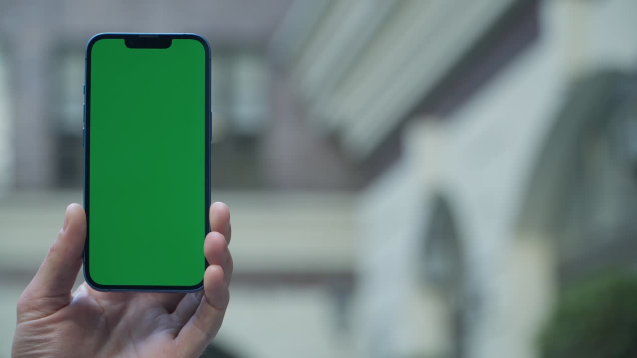 close-up de 4k de la mano de un hombre sosteniendo un teléfono inteligente con pantalla verde en una calle de la ciudad