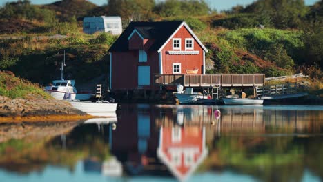 a charming red house by the water, with boats docked nearby and reflections in the calm water