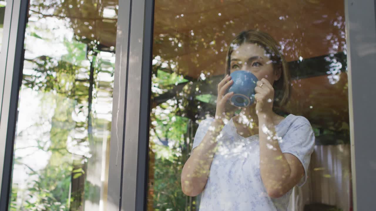 아시아 여성 이 창문 을 통해 보고 커피 를 마시고 있다