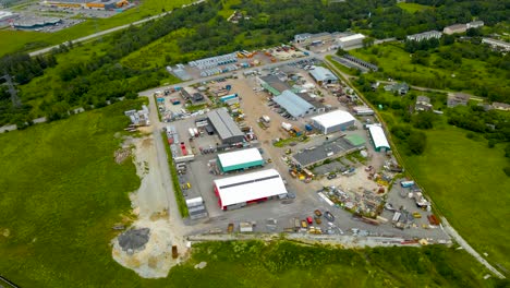 high altitude aerial drone footage orbiting around a countryside car park or an idustrial area that is fenced off from a highway and summwe green nature around it. big warehouses and rooftops visible