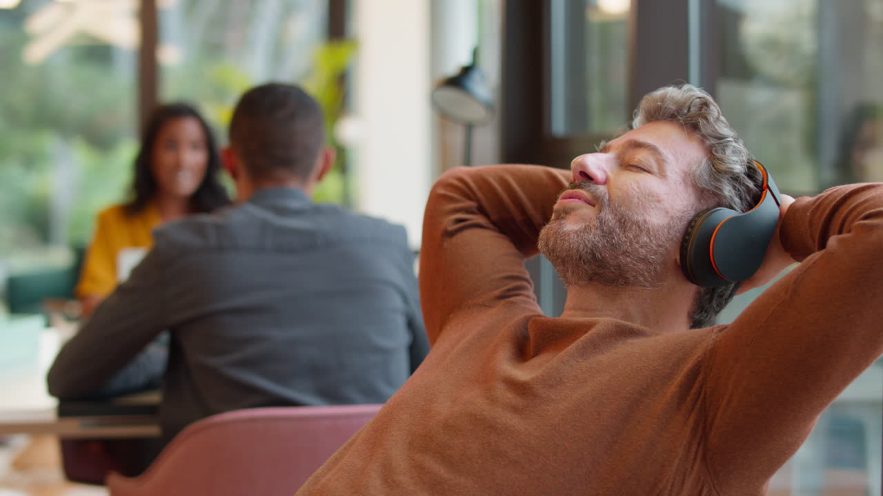 사무실에서 책상 위에 발을  ⁇ 고 무선 헤드폰으로 음악을 듣는 성숙한 사업가