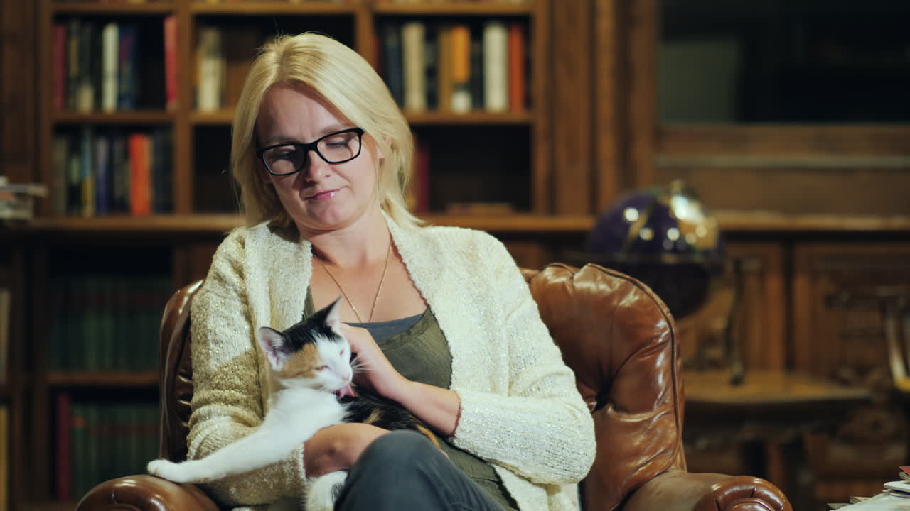 한 여성이 사무실의 고급스러운 의자에 앉아 무릎에 있는 고양이를 바라보고 있다