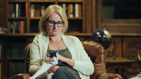 a woman sits in a luxurious chair in the office looking at a cat in her lap