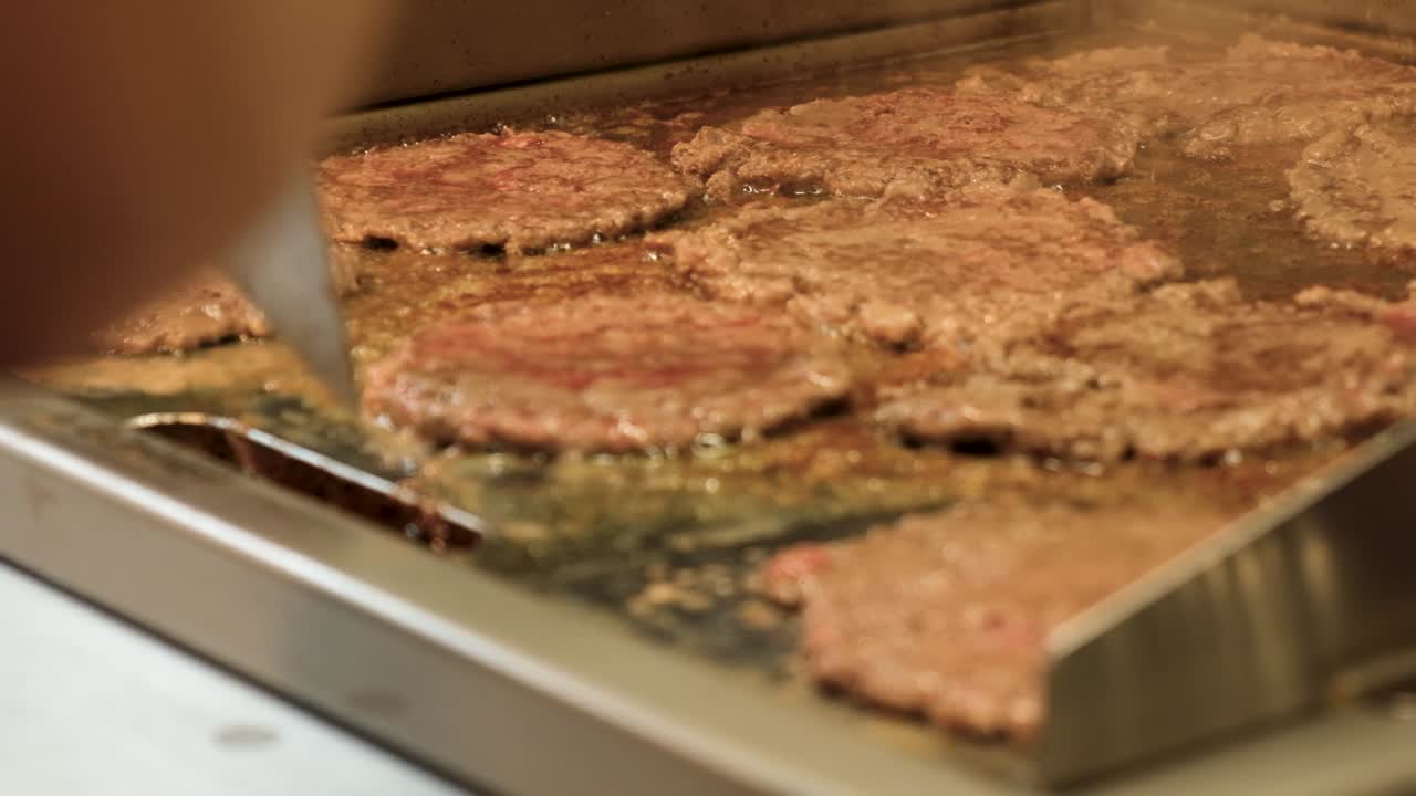 Beobachten Sie, wie saftige Rindfleisch-Patties auf einem heißen Grill in Zeitlupe für ein rauchiges, zischendes Fest garen