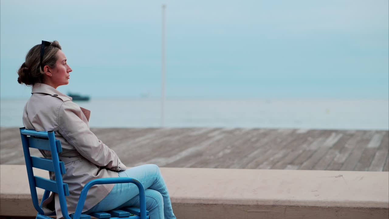 Woman in a trench coat sitting on a chair at the beach in France