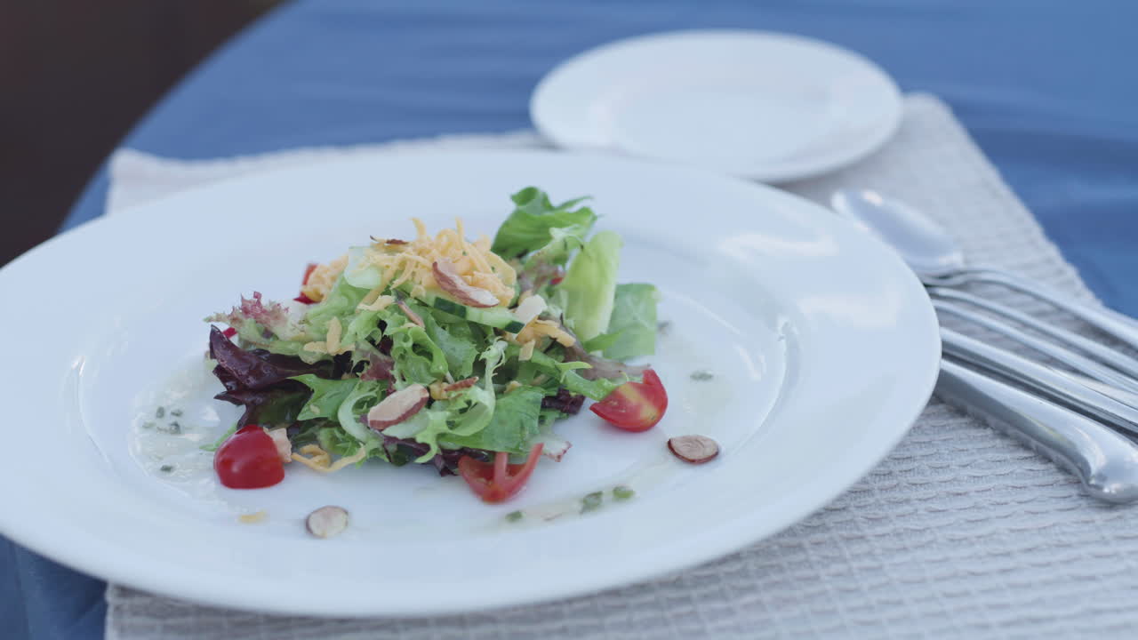 Färsk sallad på vit tallrik, utomhusbord med blå duk.