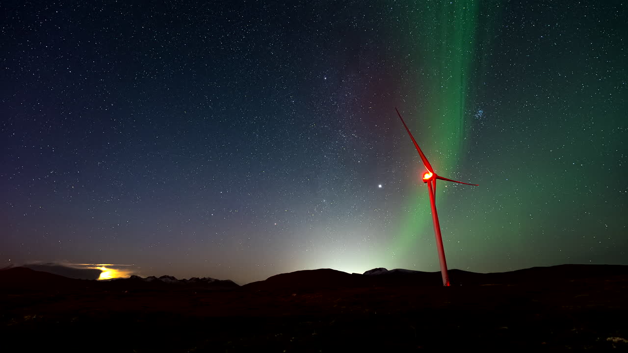 View of wind turbine with Northern Lights and satellites in night sky, timelapse