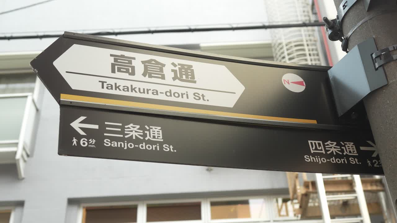A close-up of a Takakura-dori street sign in Kyoto, Japan, displaying clear directions to Sanjo-dori and Shijo-dori streets.