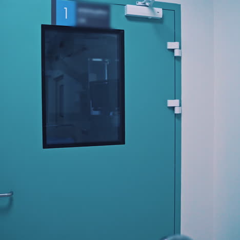 blue door of the operating room and medical cart for carrying injured patients. empty light corridor and a new gurney in the clinic indoors. motion camera back.