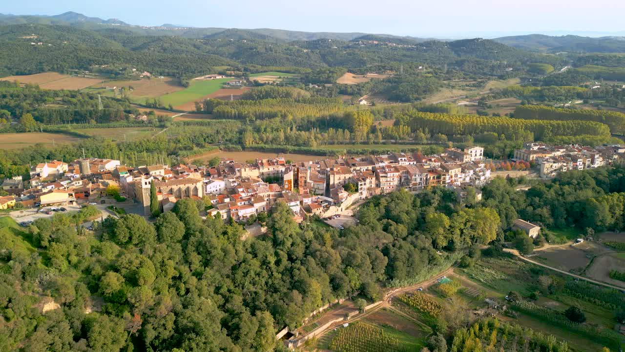 imágenes aéreas de hostalric ciudad medieval en cataluña castillo turístico en la cima de la montaña acercándose al pueblo con campos de árboles cultivados en el fondo silvicultura