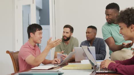 happy diverse male friends talking and using laptop in living room